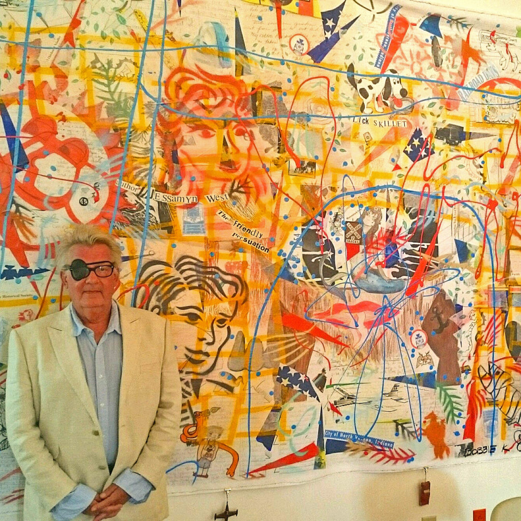 Artist standing in front of abstract mural featuring blues, reds, greens, yellows
