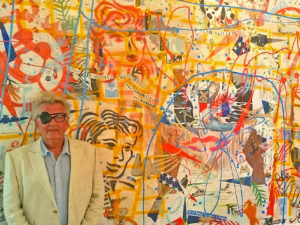 Artist standing in front of abstract mural featuring blues, reds, greens, yellows