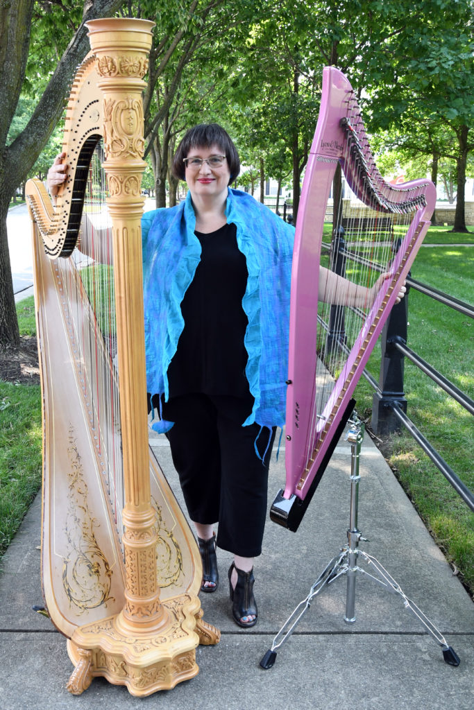 Woman smiling and holding two large harps on the sidewalk