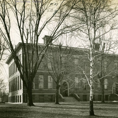 black and white photograph of a 3-story brick and stone building with arched doorways